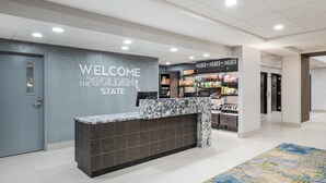 Un espace d’accueil d’hôtel avec un comptoir en marbre, un panneau d’accueil et un présentoir de collations.