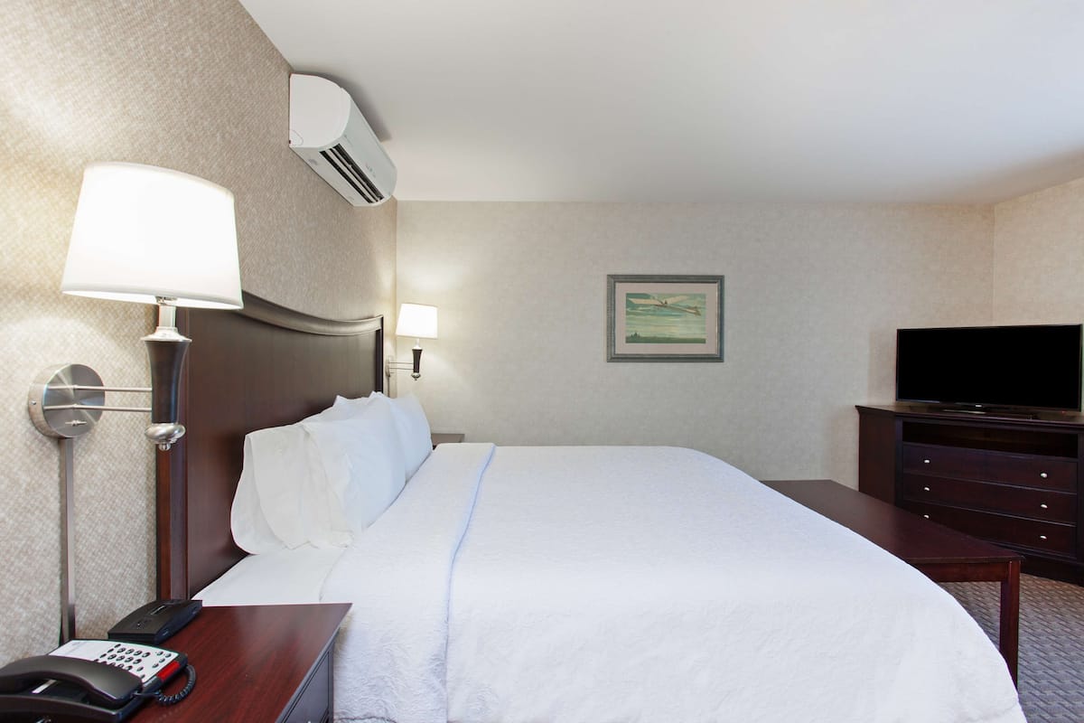Een hotelkamer met een bed, bedlamp, telefoon, airconditioning en een dressoir.