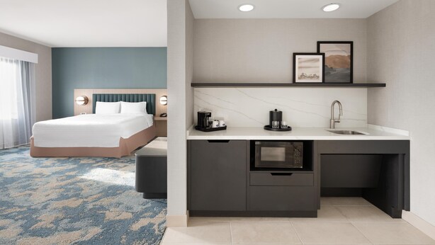 Une chambre d’hôtel moderne équipée d’un lit, d’une petite kitchenette et d’une salle de bain.