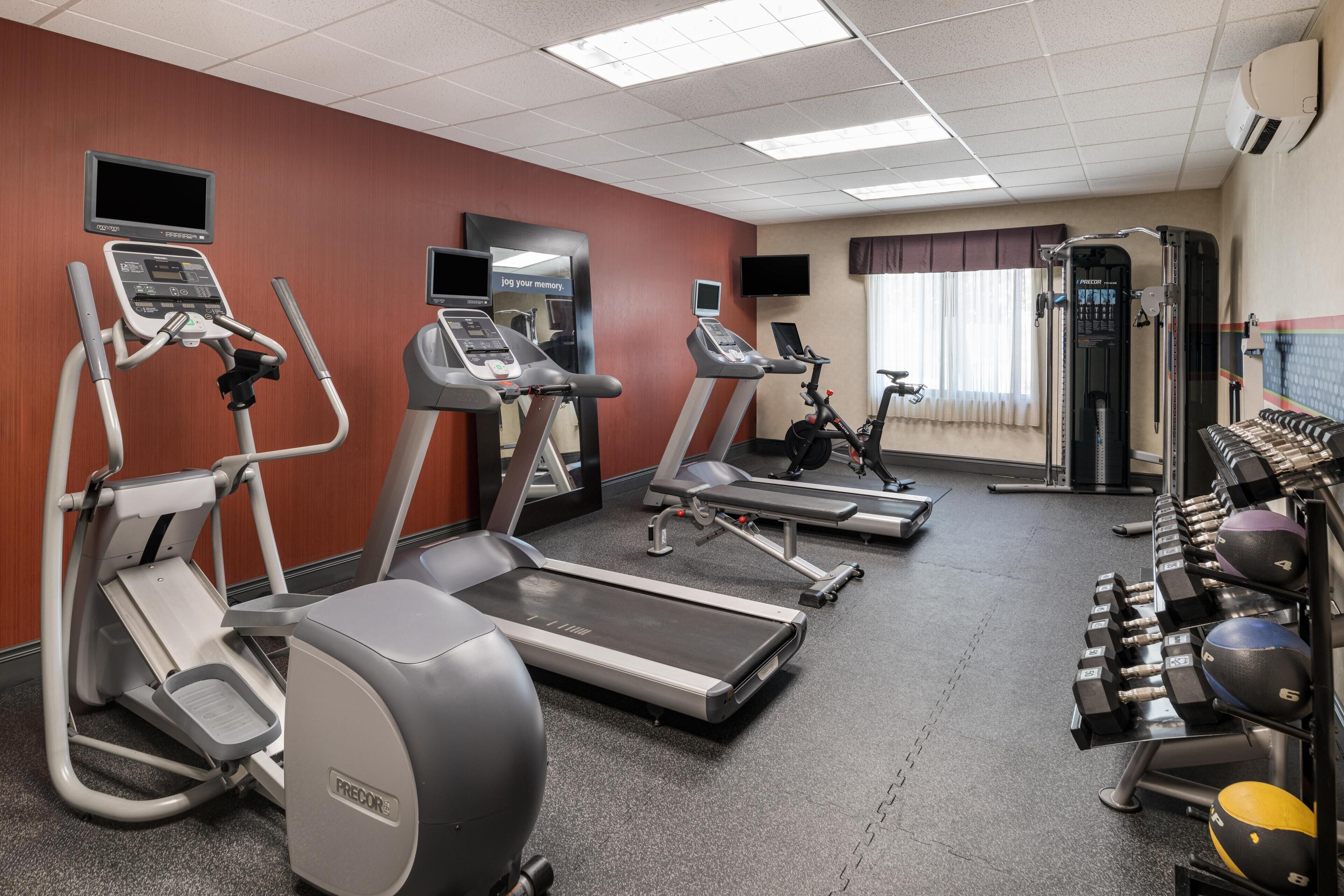Ein Fitnessstudio mit Laufbändern, Ellipsentrainern, einem Ergometer und Kurzhanteln.