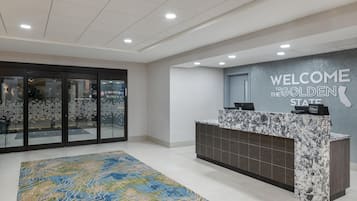 A hotel reception area with a marble counter, a welcome sign, and a patterned rug.
