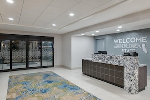 A hotel reception area with a marble counter, a welcome sign, and a patterned rug.
