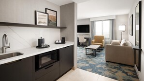 Une chambre d’hôtel moderne dotée d’un coin cuisine, d’un canapé, d’une télévision et d’un téléviseur à écran plat fixé au mur.