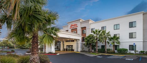 A Hampton Inn & Suites hotel with a clear entrance, parking lot, and surrounding palm trees.