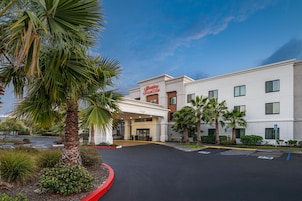 Un hotel Hampton Inn & Suites con entrada despejada, estacionamiento y palmeras circundantes.