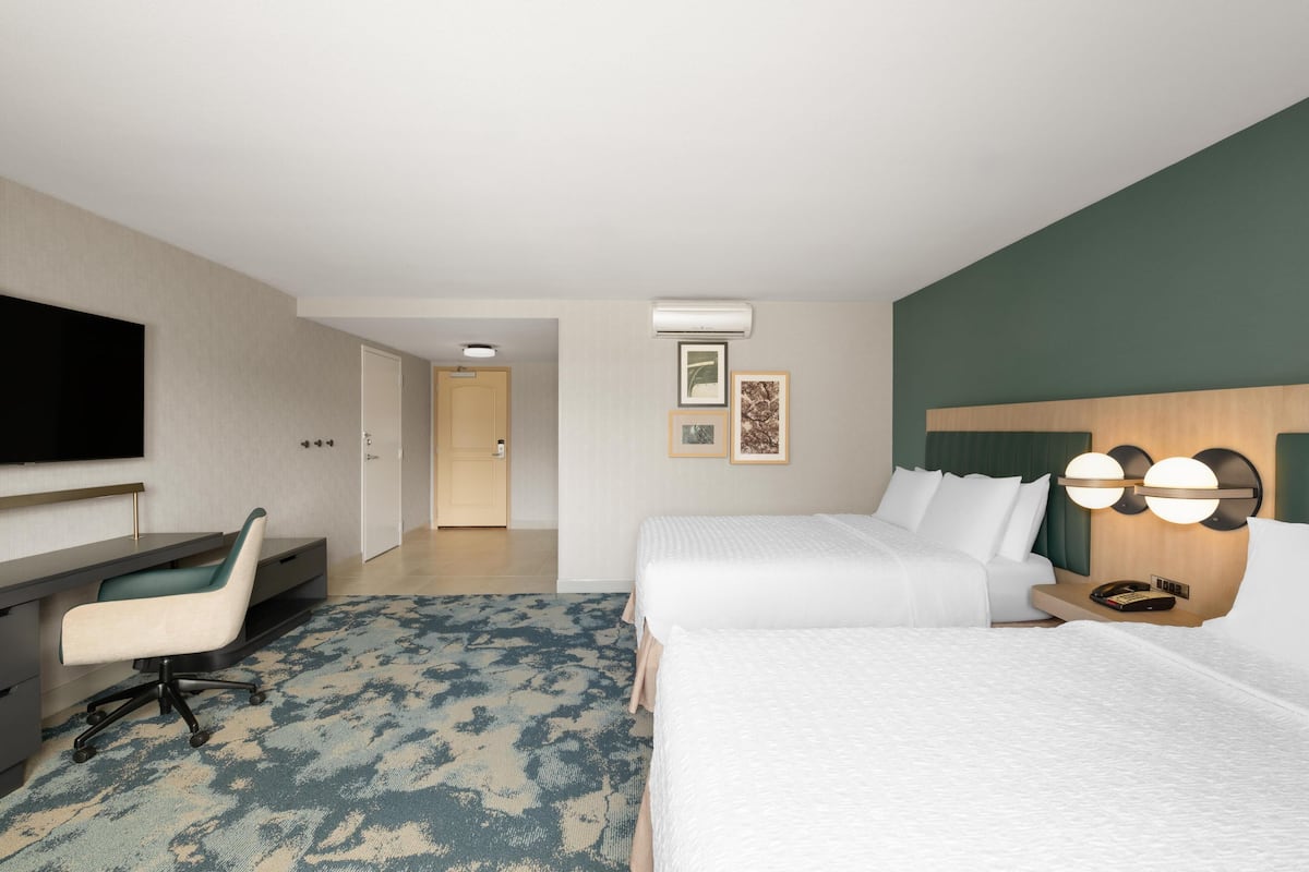 Een hotelkamer met een bed, een bureau, een stoel, een televisie en een wandlamp.