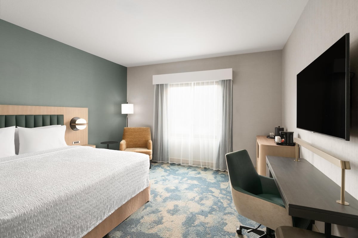 Een hotelkamer met een bed, een bureau, een stoel, een televisie en een raam met gordijnen.