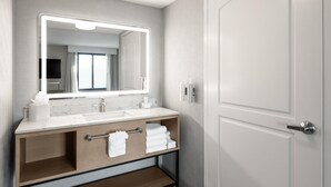 Une salle de bain moderne avec un grand miroir, deux lavabos, un meuble-lavabo avec rangements et une porte.