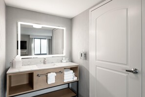 A modern bathroom with a large mirror, two sinks, a vanity with storage, and a door.