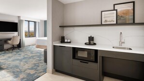 Une chambre d’hôtel moderne dotée d’une kitchenette, d’un téléviseur à écran plat, d’un bureau et offrant une vue sur l’extérieur.