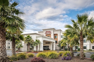 Un hotel con entrada despejada, palmeras y un letrero de Hampton Inn & Suites.