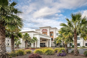 A hotel with a clear entrance, palm trees, and a sign for Hampton Inn & Suites.