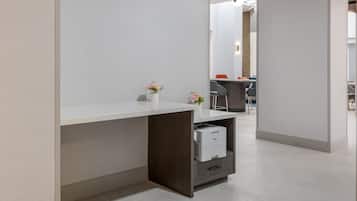 A modern office space with a white desk, a small shelf with a printer, and a vase with flowers.