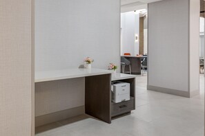Un espacio de oficina moderno con un escritorio blanco, un estante pequeño con una impresora y un florero con flores.
