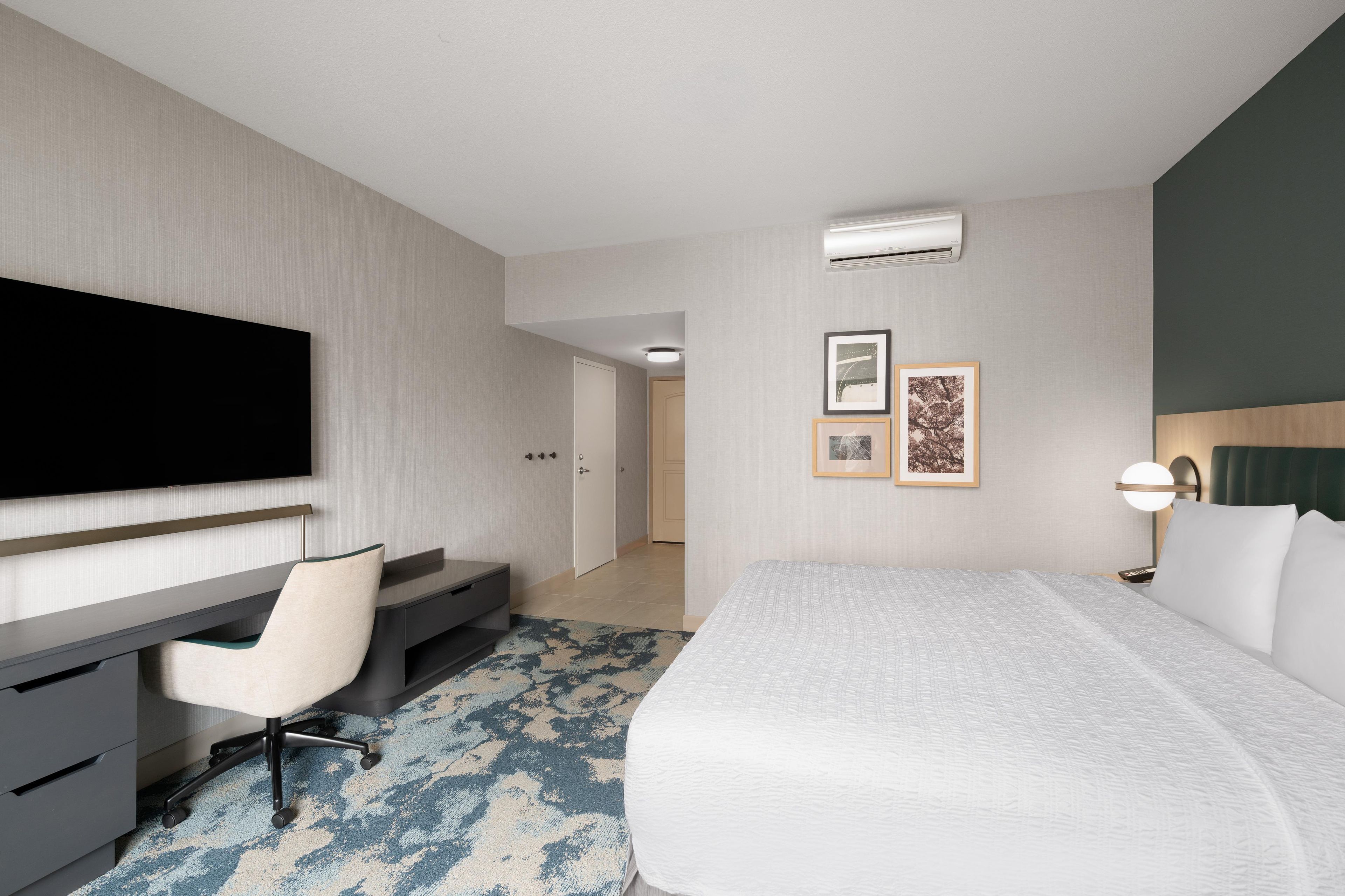 A hotel room with a bed, a desk, a chair, a television, and two framed pictures on the wall.