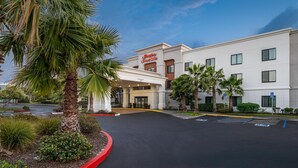 Un hôtel Hampton Inn & Suites avec une entrée bien visible, un parking et des palmiers environnants.