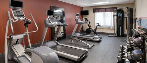 Un gimnasio con cintas de correr, elíptica, bicicleta estática y pesas sueltas.
