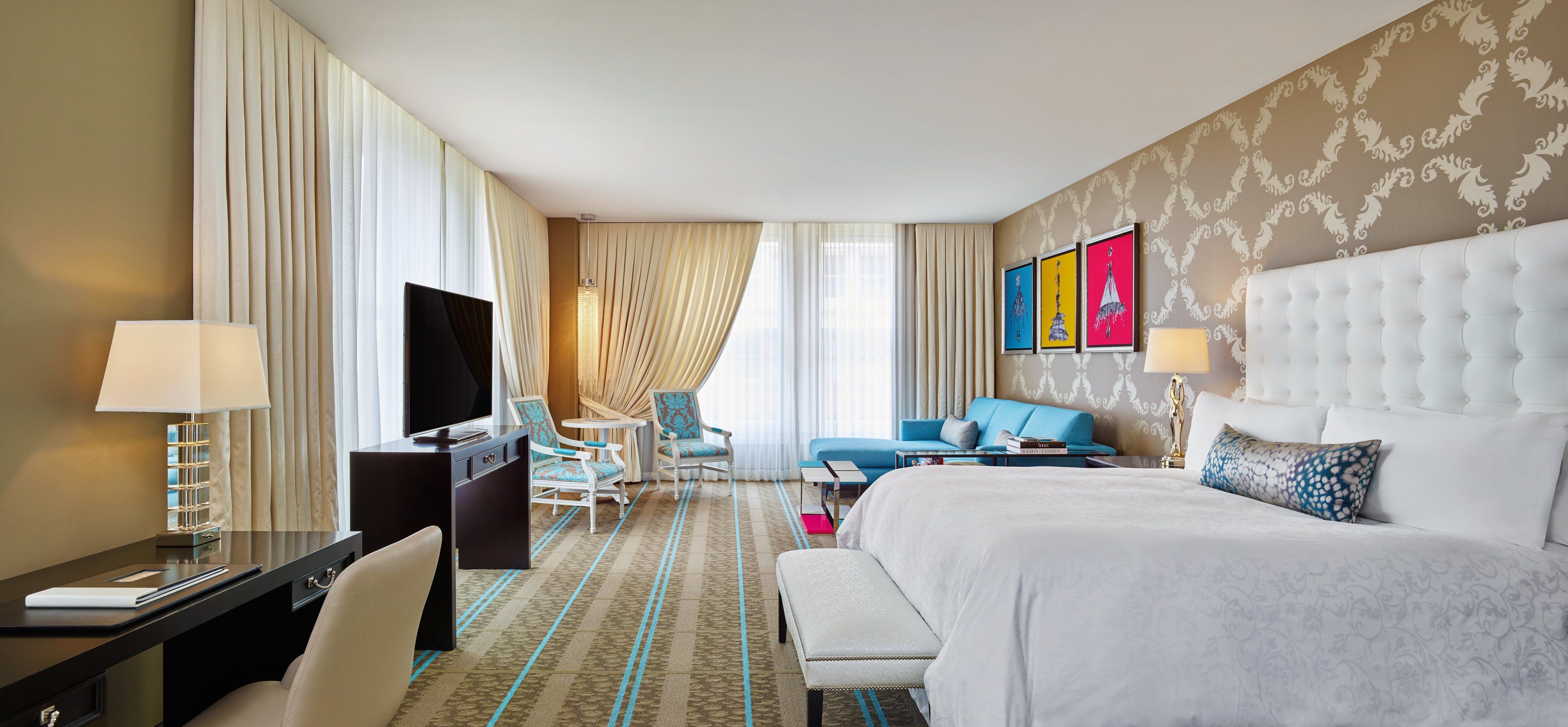 A hotel room with a large bed, a desk with a TV, a sofa, and a chair.