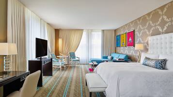 A hotel room with a large bed, a desk with a TV, a sofa, and a chair.