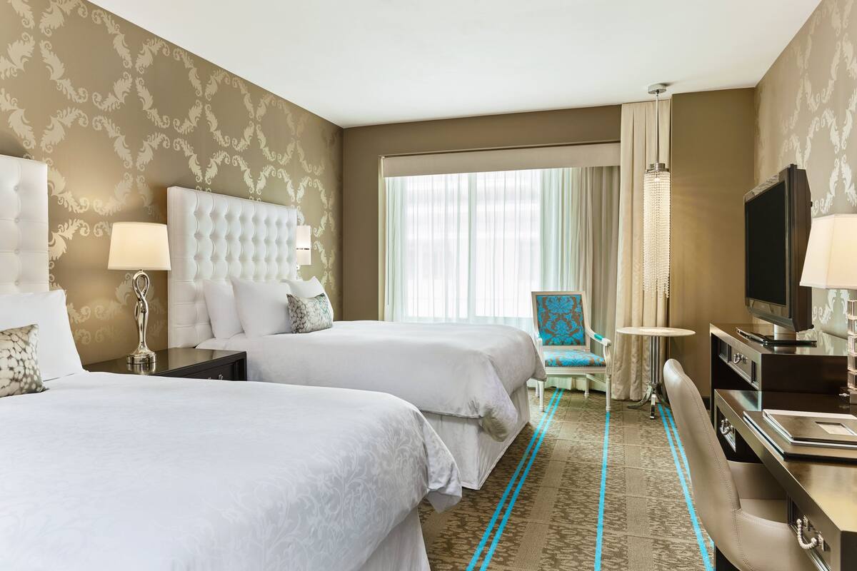 A hotel room with two beds, a TV, a desk, and a chair.