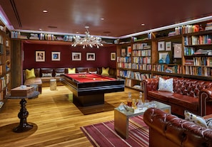 A library with a pool table, leather sofas, and bookshelves filled with books.