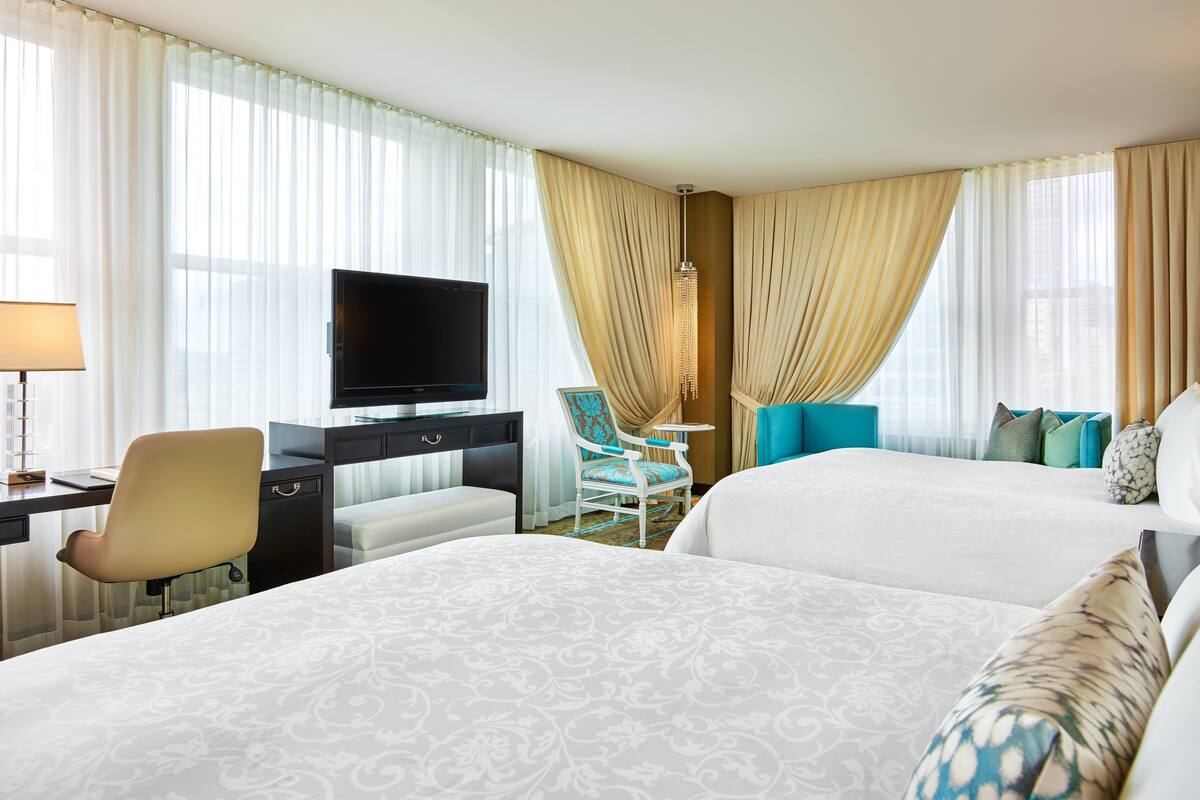 A hotel room with two beds, a desk with a TV, a chair, and a small table.