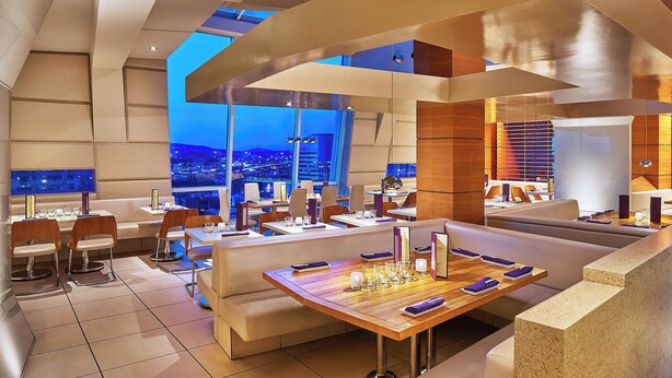 A modern restaurant with high ceilings, large windows, and a view of the cityscape at dusk. - The Nines, a Luxury Collection Hotel, Portland (Portland)