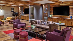 A modern living room with a large flat-screen TV, wooden ceiling beams, a fireplace, and a bookshelf. - The Nines, a Luxury Collection Hotel, Portland (Portland)