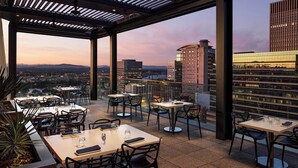 An outdoor dining area with tables and chairs, large windows, and a view of the cityscape. - The Nines, a Luxury Collection Hotel, Portland (Portland)