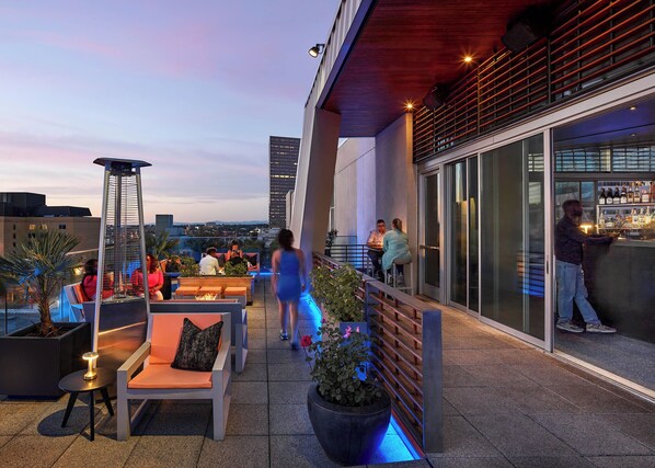 A rooftop bar with outdoor seating, a bar area, and a view of the city skyline.