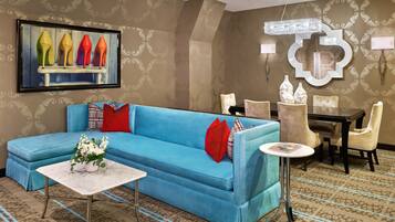 A living room with a blue sofa, a small table with a vase of flowers, and a dining area with chairs and a table.