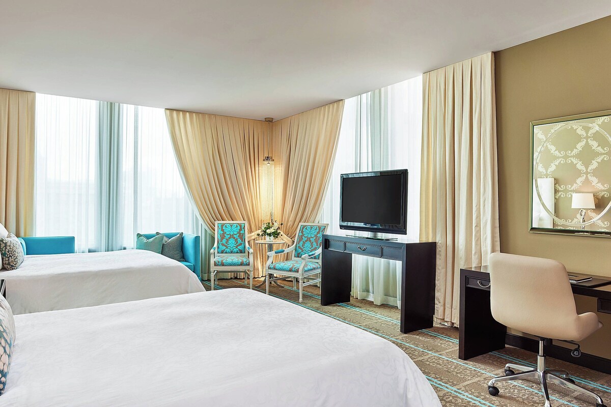 A hotel room with two beds, a desk with a TV, and a seating area with chairs.