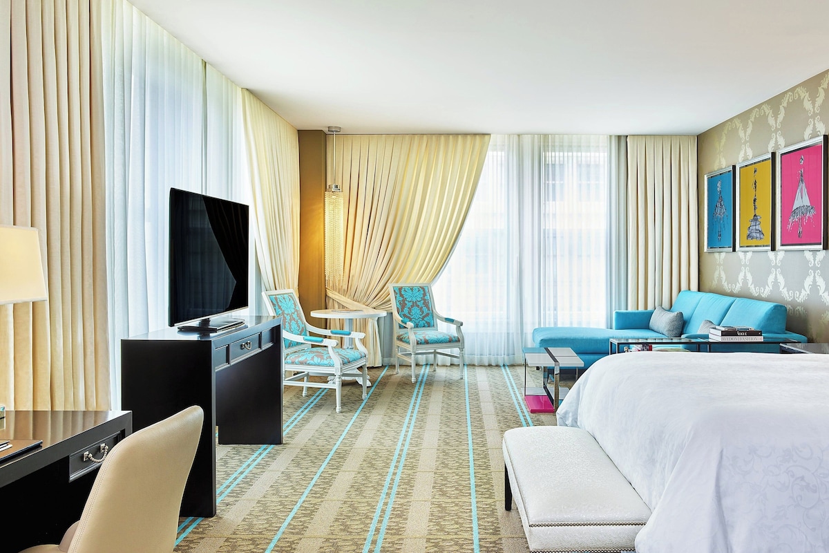 A hotel room with a large bed, a desk with a TV, two armchairs, a sofa, and a patterned carpet.
