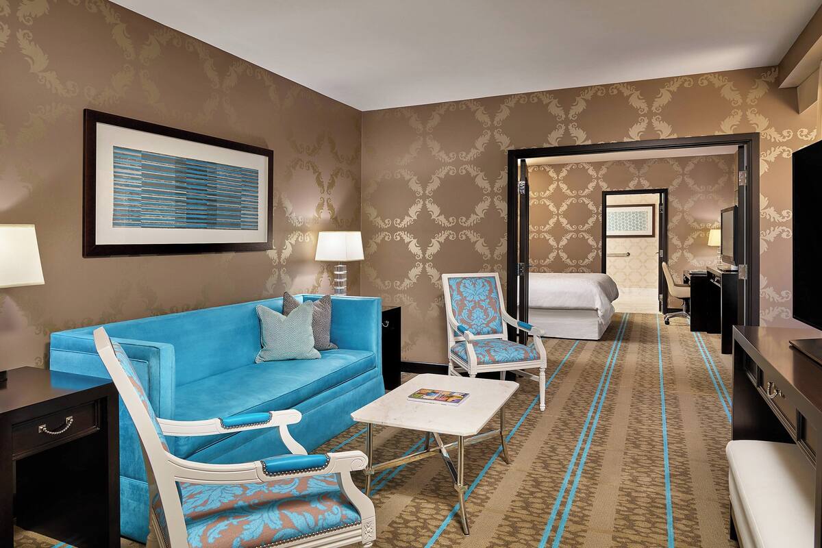 A hotel room with a blue sofa, a white armchair, a small white table, and a bed.