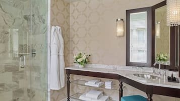 A bathroom with a glass-enclosed shower, a marble sink, and a vanity with a mirror and sconces.