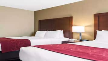 Quarto de hotel com duas camas, uma mesa de cabeceira, um abajur e um tapete estampado.