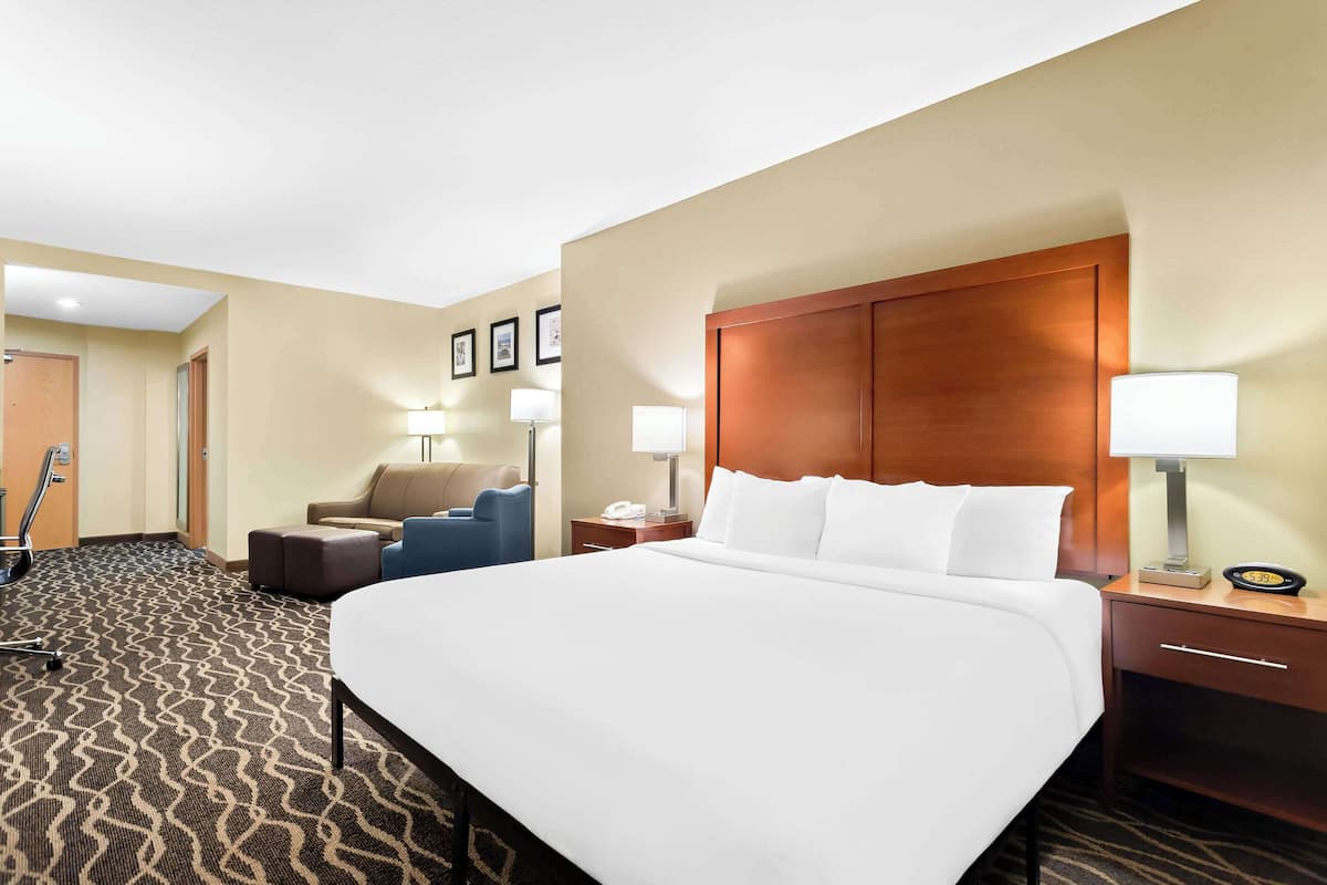 Ein Hotelzimmer mit einem großen Bett, einem Schreibtisch mit Lampe, einem Sessel und einem kleinen Tisch mit Telefon.