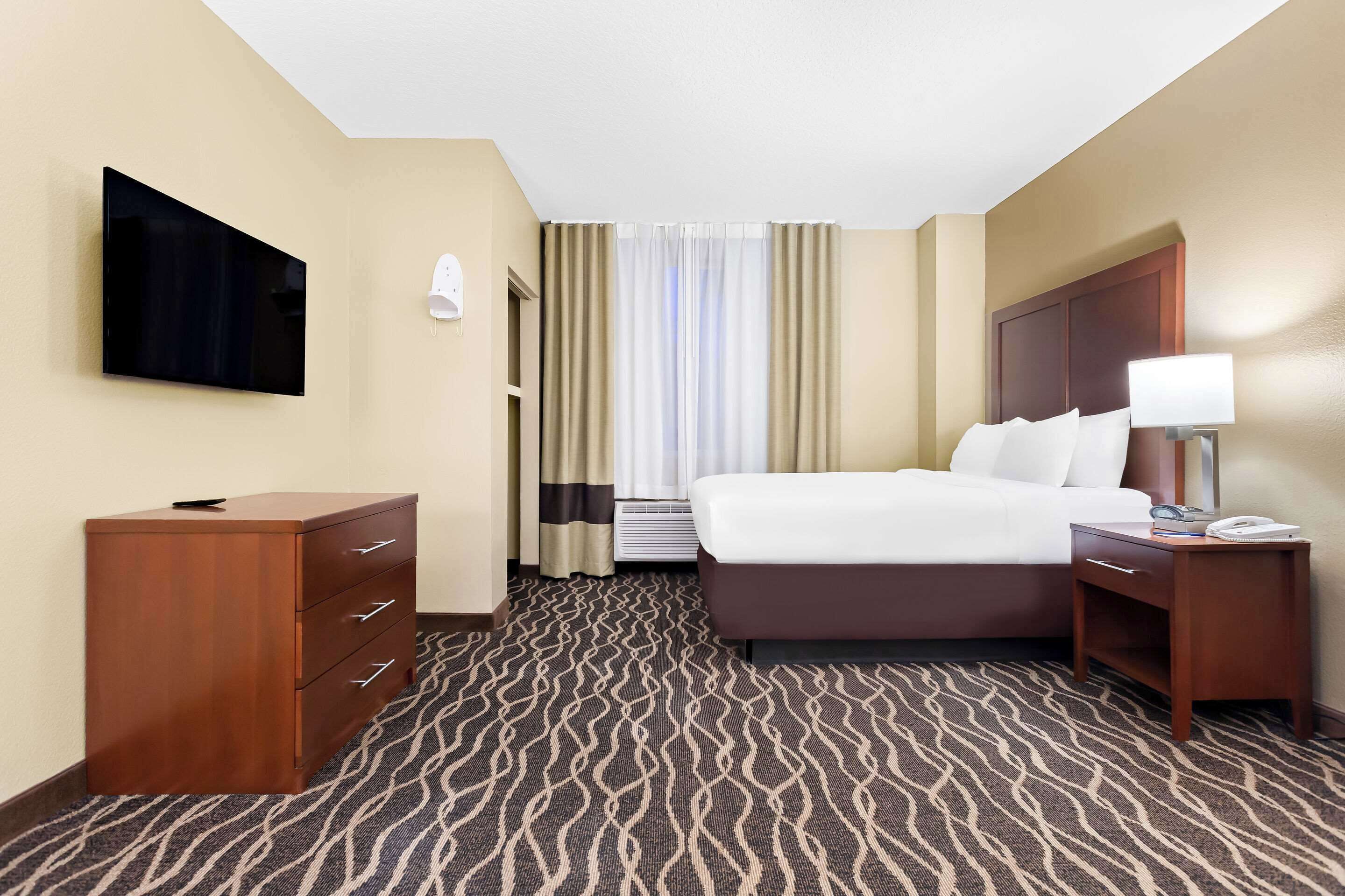 Quarto de hotel com cama, televisão na parede, escrivaninha e abajur.