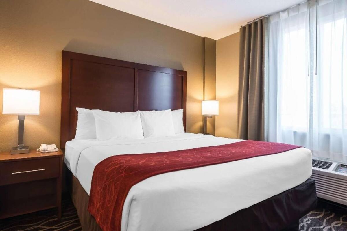 Ein Hotelzimmer mit einem großen Bett, zwei Nachttischlampen, einem Nachttisch und einem Fenster mit Vorhängen.