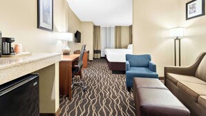 Ein Hotelzimmer mit Küchenzeile, einem Bett, einem blauen Sessel, einem braunen Sofa und einem gemusterten Teppich.