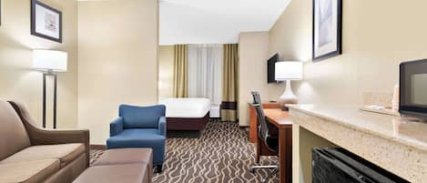 Une chambre d’hôtel équipée d’un canapé, d’un fauteuil bleu, d’un lit, d’un bureau, d’une télévision et d’un mini-bar.