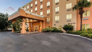 Ein Hotel mit Eingangsbereich, überdachtem Gang, Parkplatz und umliegendem Grün.