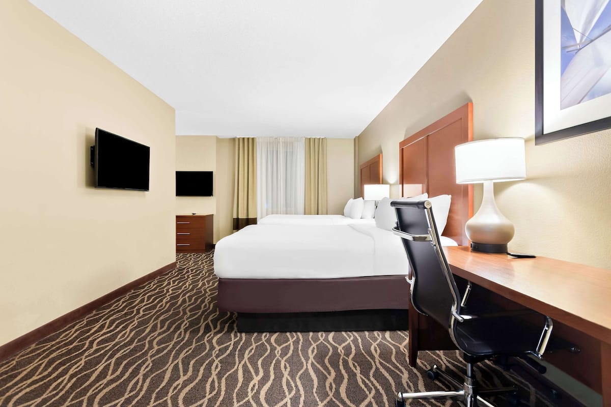 Ein Hotelzimmer mit einem großen Bett, einem Schreibtisch mit Stuhl, einem flachbildfernseher an der Wand und einer Schreibtischlampe.