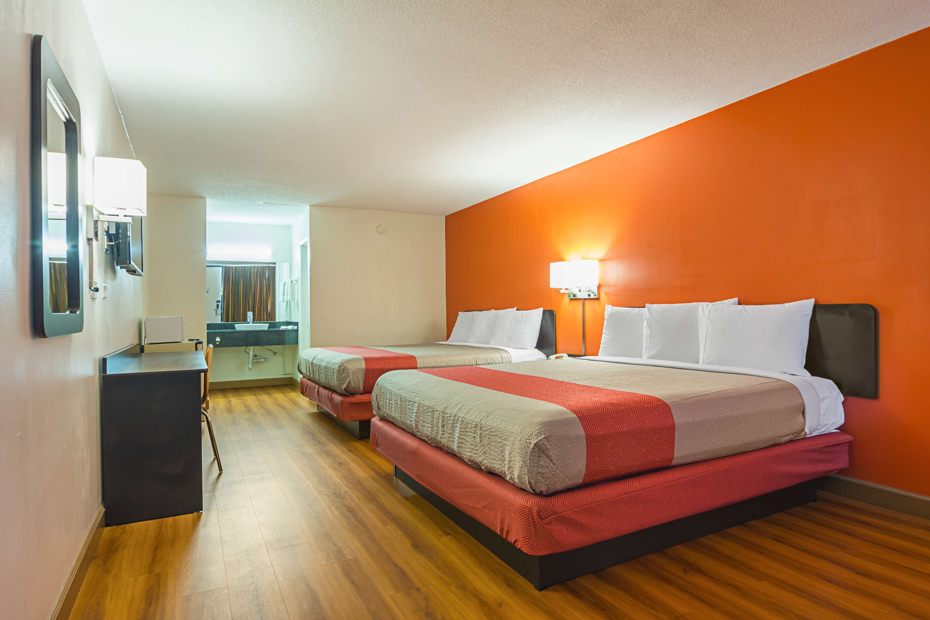 A hotel room with two beds, a desk, and a bathroom visible in the background.