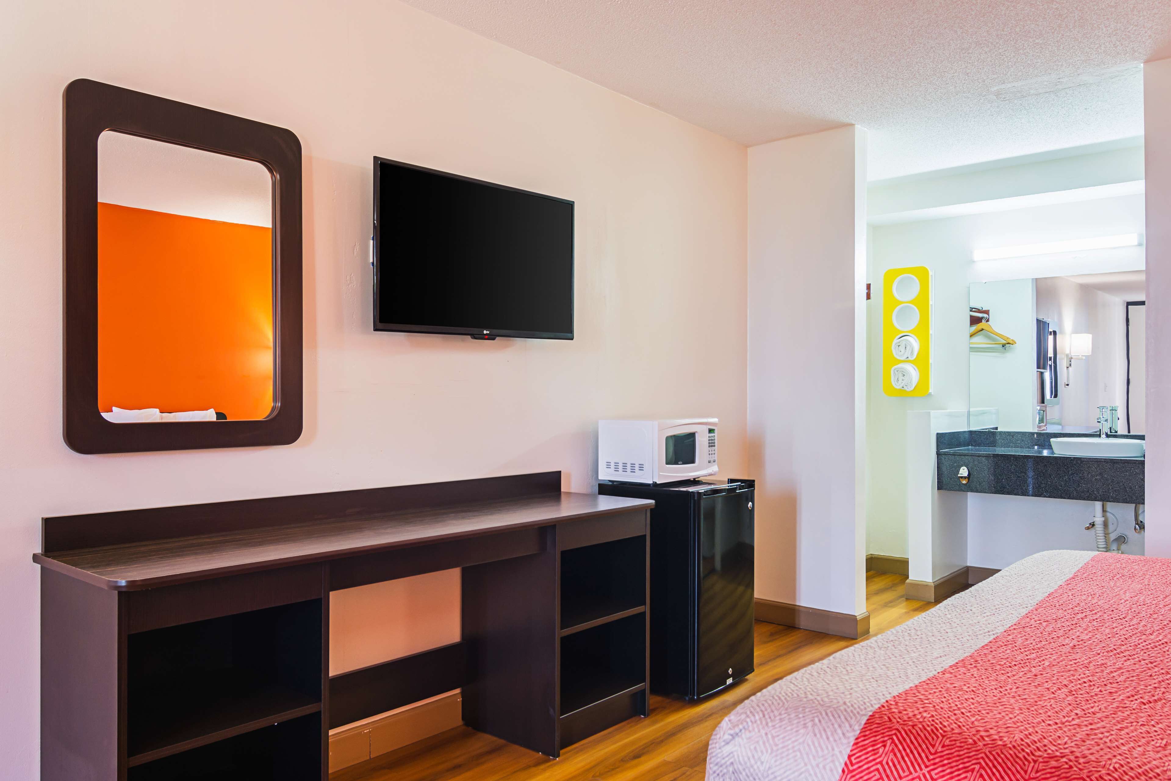 A hotel room with a bed, a TV, a desk with a microwave, and a bathroom with a mirror and sink.