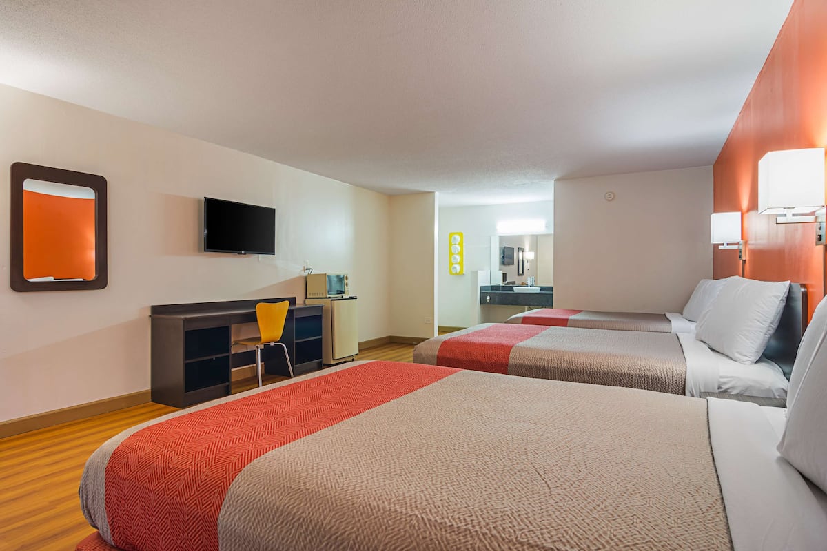A hotel room with two beds, a desk, a chair, a TV, and a mirror.