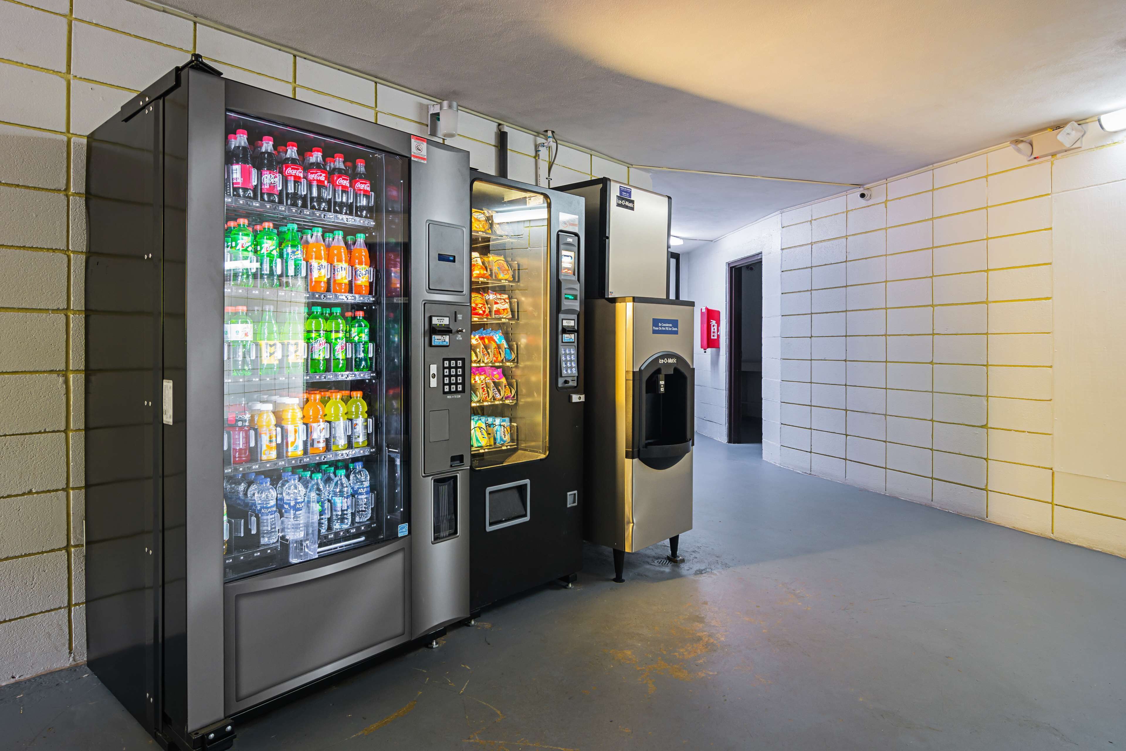 A row of vending machines in a hallway with tiled walls and a concrete floor.