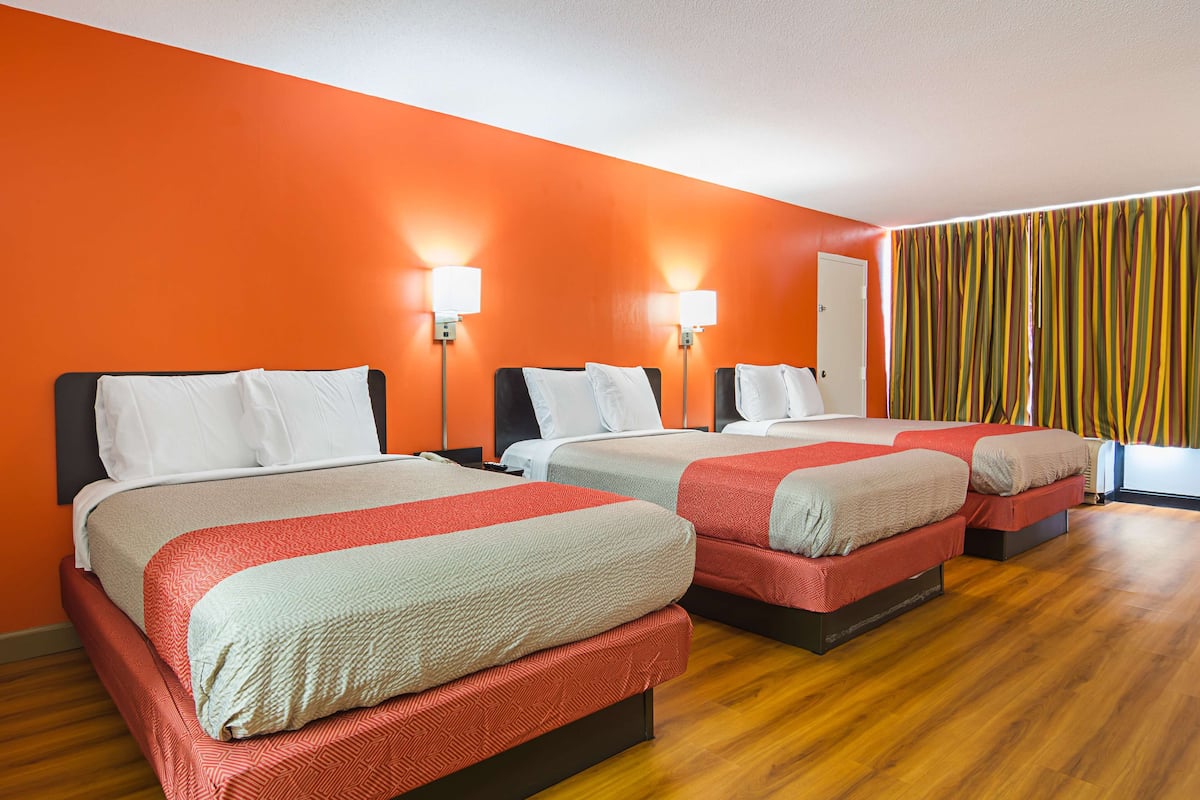A hotel room with three beds, orange walls, and wooden flooring.