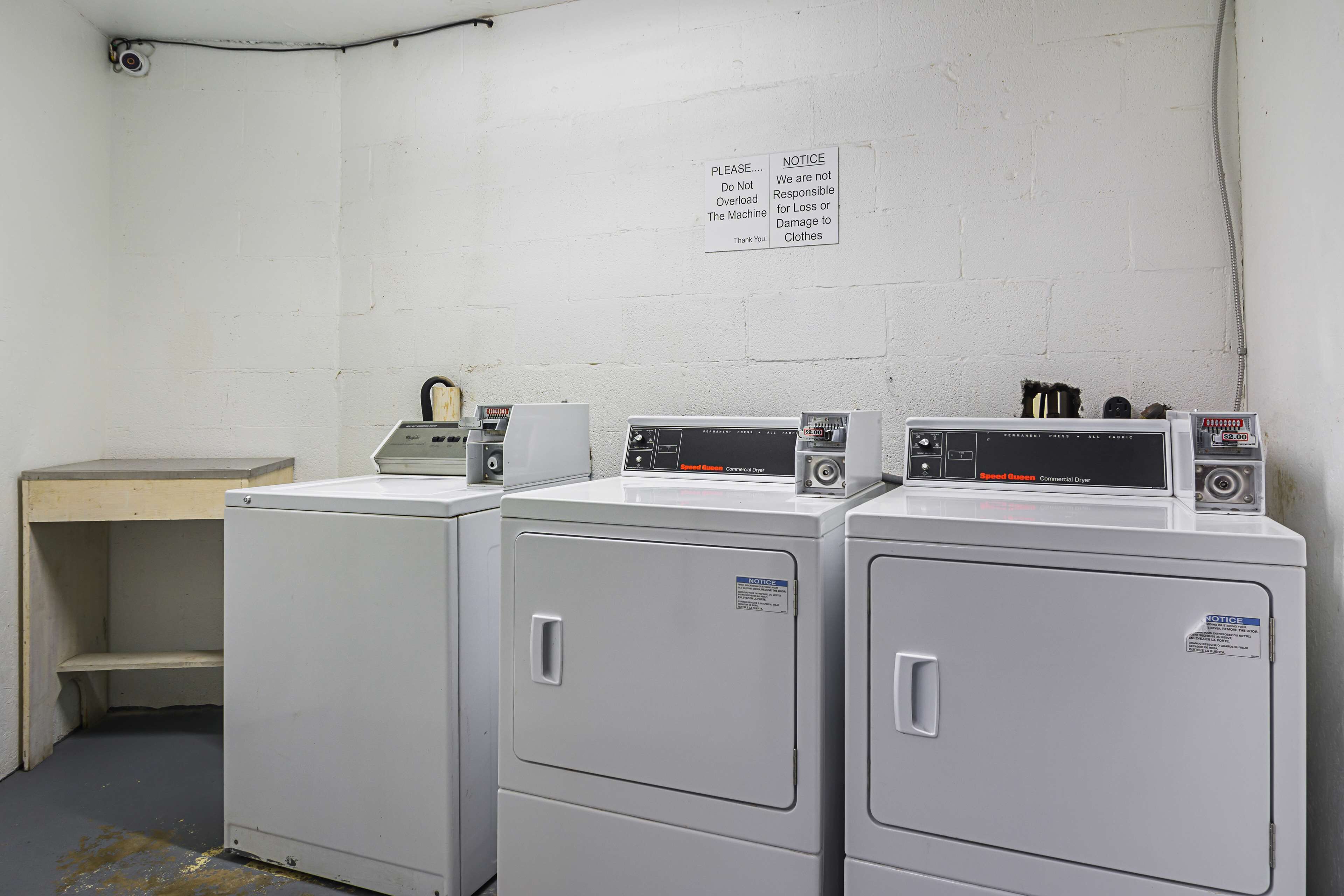 A laundry area with three stacked washers and dryers, a white wall with a notice, and a wooden bench.