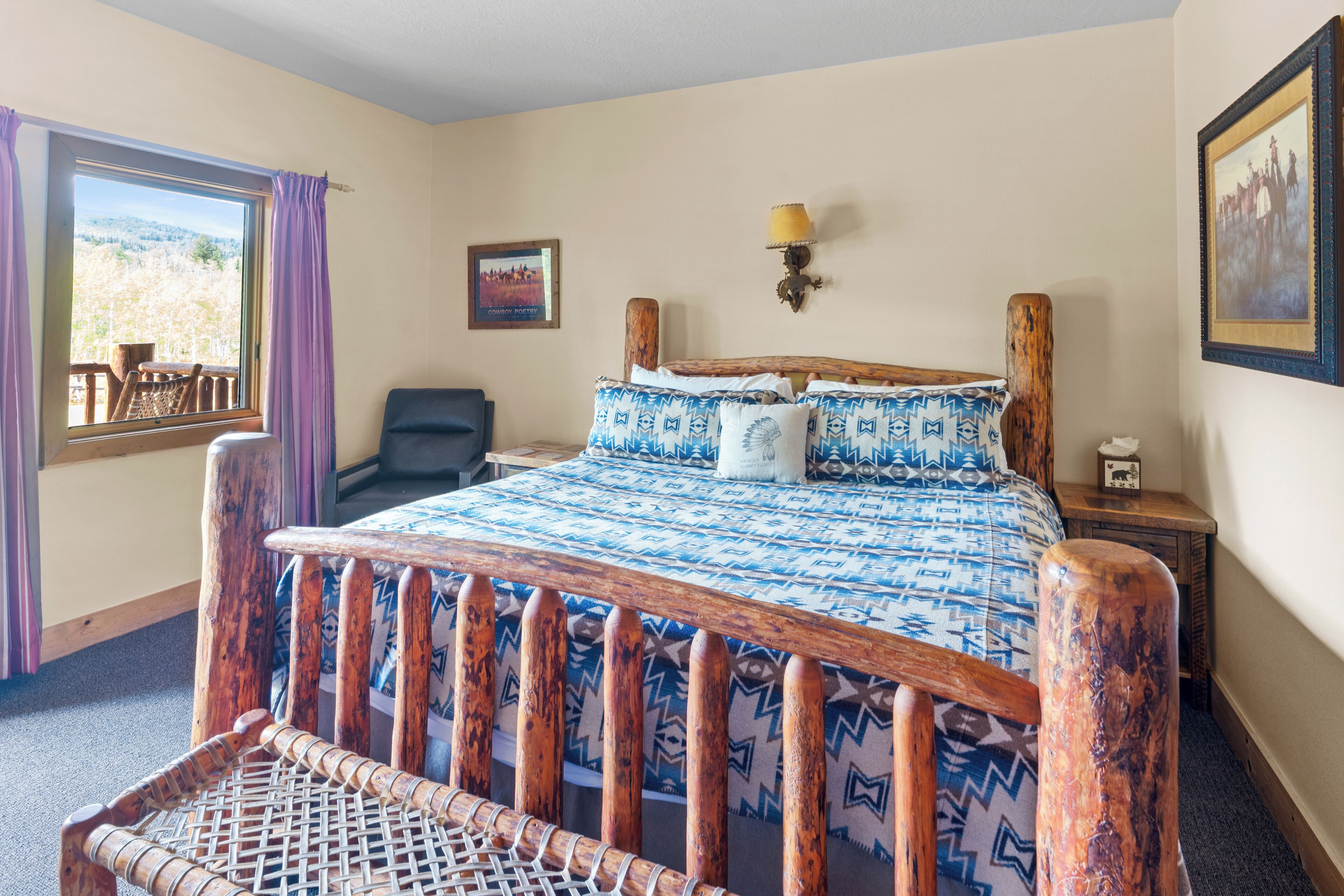 Quarto com cama de madeira, uma cadeira, mesa de cabeceira, luminária e janela com cortinas.
